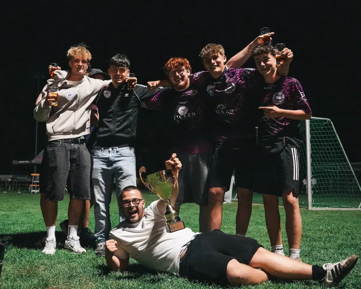 Zwei Spieler sitzen im Gras, einer hält den Pokal