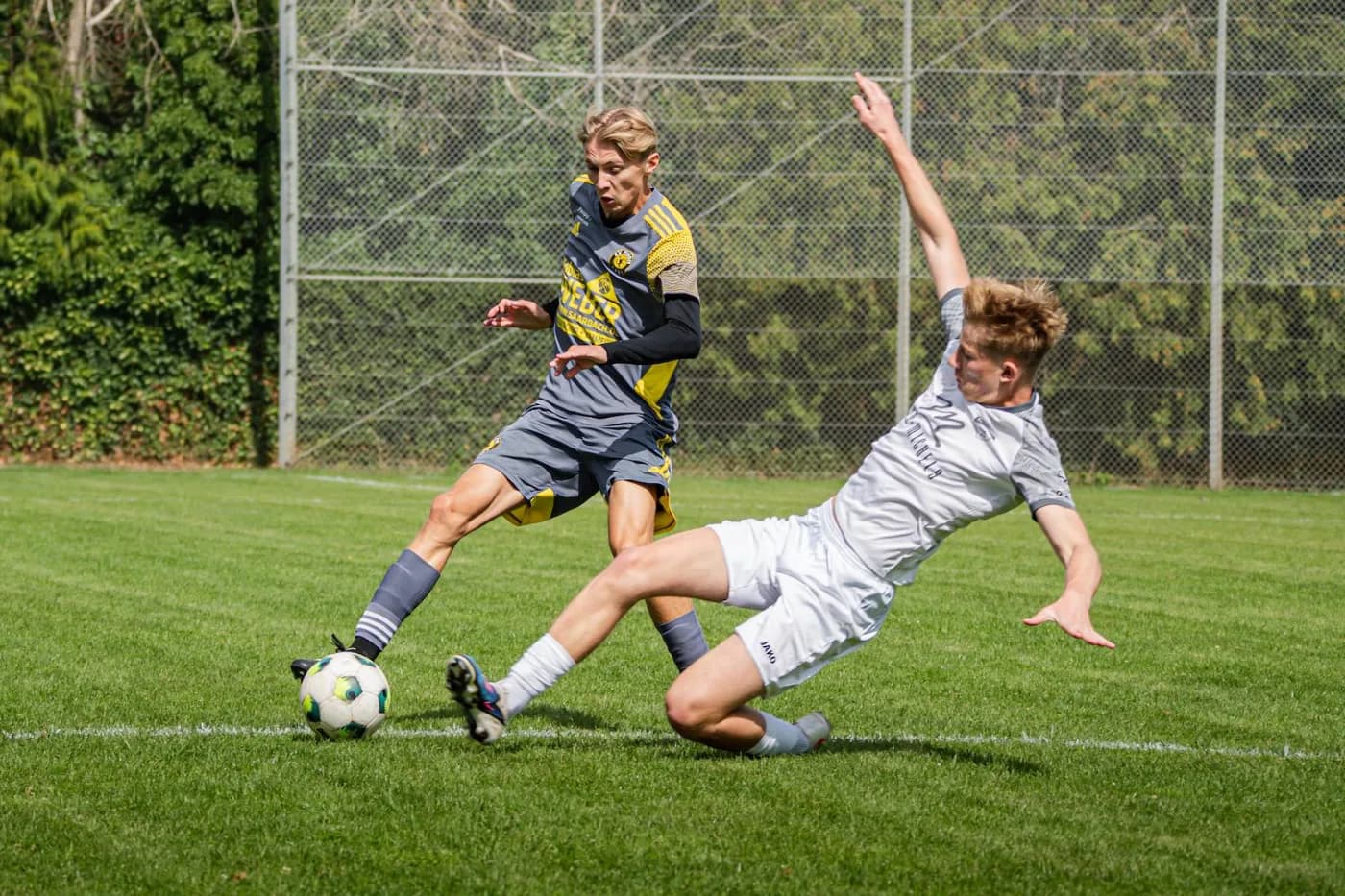 Ein Spieler grätscht in den Ball, der Gegenspieler kommt zu Fall