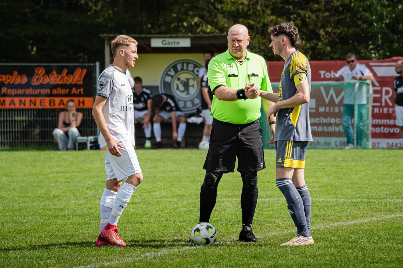 Der Schiedsrichter steht zwischen zwei Spielern am Spielfeldrand