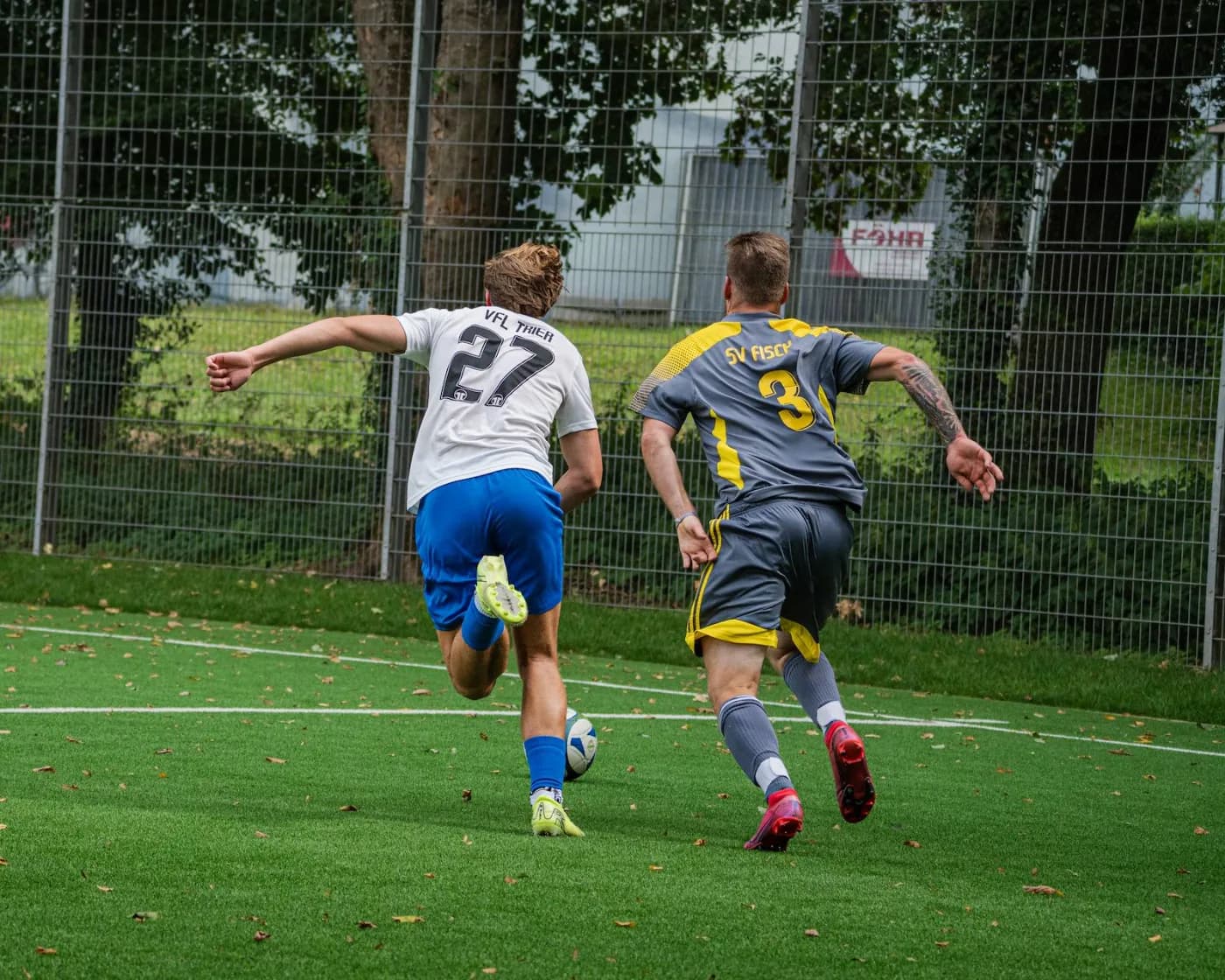 Zwei Spieler sprinten dem Ball hinterher, von hinten aufgenommen