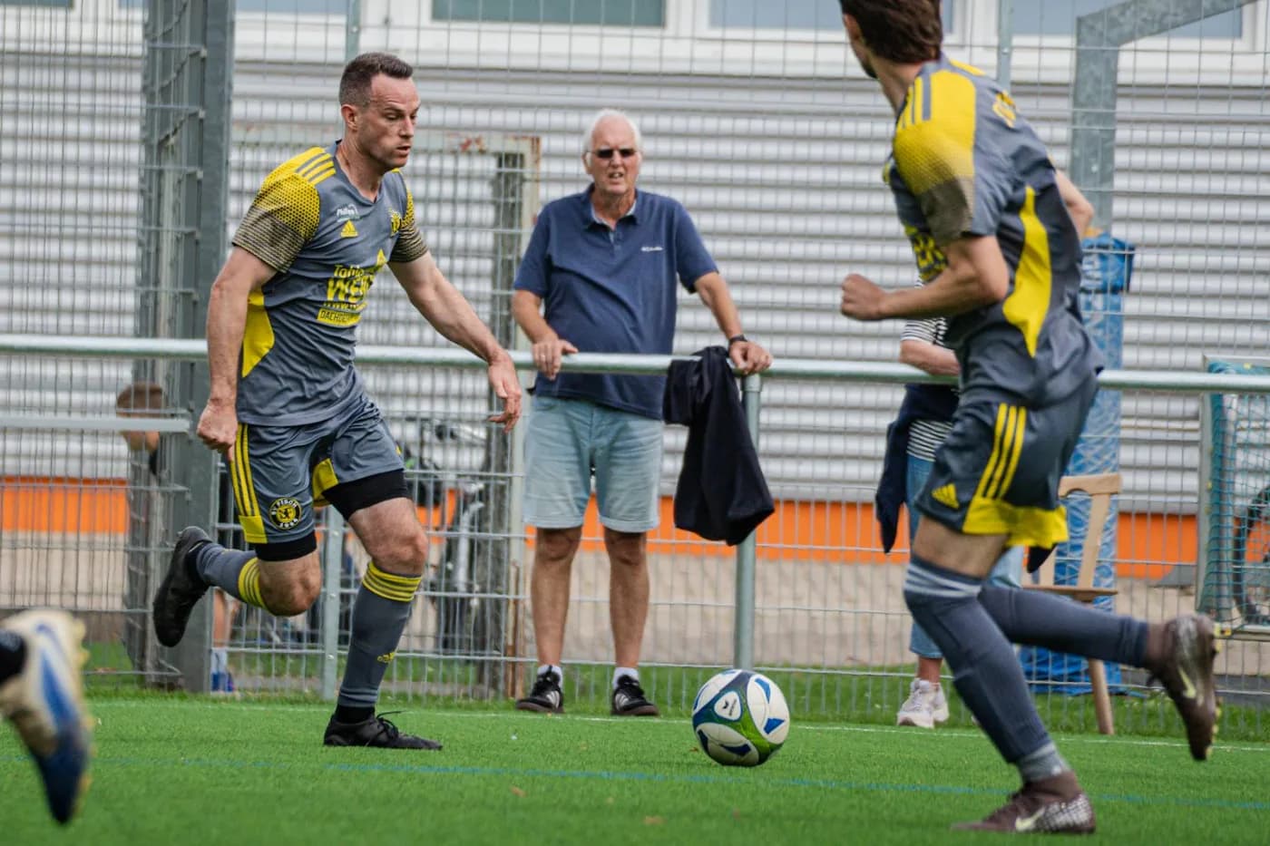 Ein Spieler zieht mit dem Ball an der Bande vorbei, dahinter sitzen Zuschauer